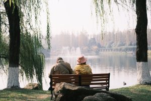 Elderly couple enjoying a peaceful moment by a lake in a serene park setting.